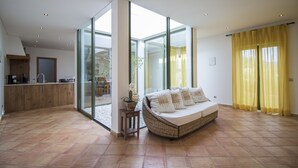 A modern living room with a sofa, a small table, and a kitchen area visible through glass doors. - Casa Serena | 6 Bedrooms | Country House |  Estoi (Estoi)