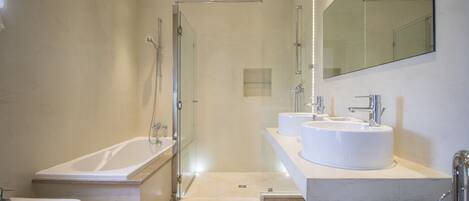 A modern bathroom with a glass-enclosed shower, a freestanding bathtub, and a vanity with two sinks.