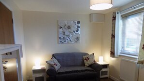 A cozy room with a grey sofa, two bedside tables with lamps, a radiator, and a window with curtains. - A Home From Home 3 (Plymouth)