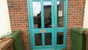 A turquoise door with a window, flanked by green trash bins, against a brick wall. - A Home From Home 3 (Plymouth)