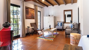 Uma sala de estar espaçosa com piso de azulejos, teto de madeira, um armário branco, um sofá, uma mesa de centro e uma mesa vermelha com um vaso.