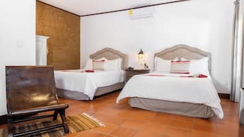 Une chambre d’hôtel avec deux lits, une chaise en bois, une table de chevet avec une lampe et un sol carrelé.