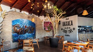 Un interior de restaurante con muebles de madera, un mural y una gran planta en maceta.