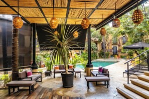 Un espace extérieur aménagé, abrité et doté de fauteuils confortables, d’une grande plante en pot et de lanternes suspendues.