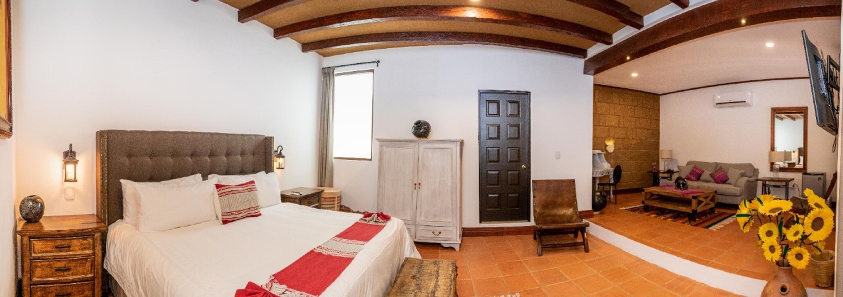 Un dormitorio con cama, armario, puerta, sillón, sofá y un florero con flores.