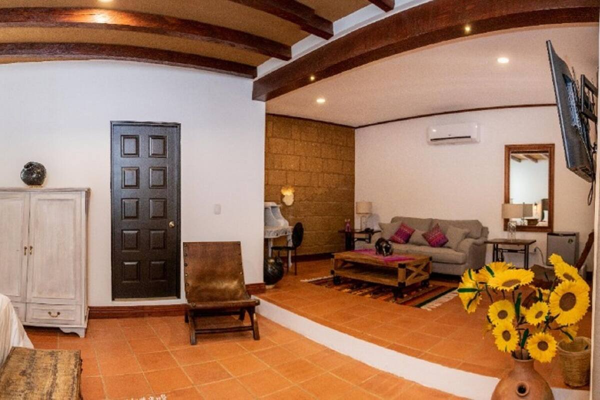 Un dormitorio con cama, armario, puerta, sillón, sofá y un florero con flores.