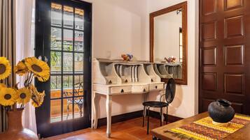 A room with a desk, chair, and a table with a vase.