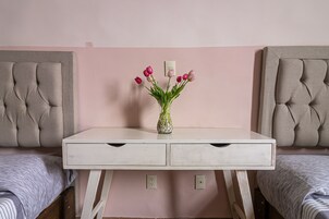 Ein Schlafzimmer mit weißem Schminktisch, zwei gesteppten Kopfteilen, einer rosa Wand und einer Vase mit Blumen auf dem Schminktisch.