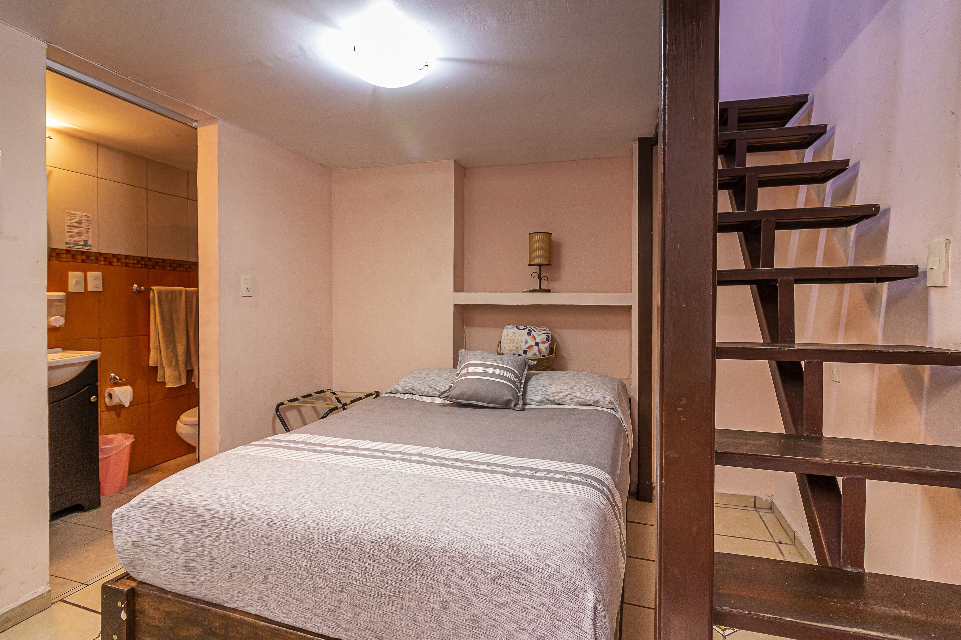 A bedroom with a bed, a nightstand, a lamp, and a staircase.