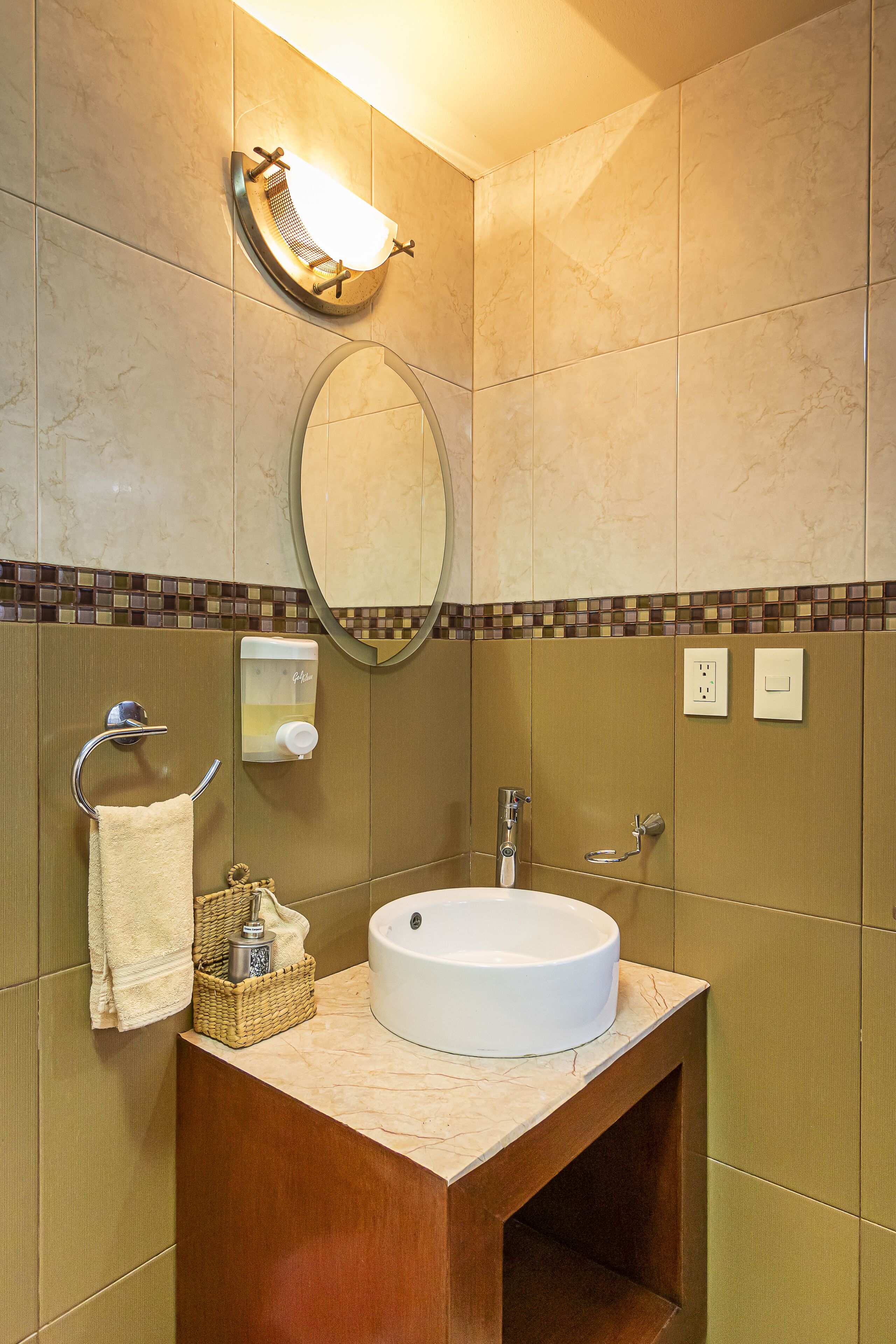 A bathroom with a round sink, a mirror, a towel rack, and a soap dispenser.