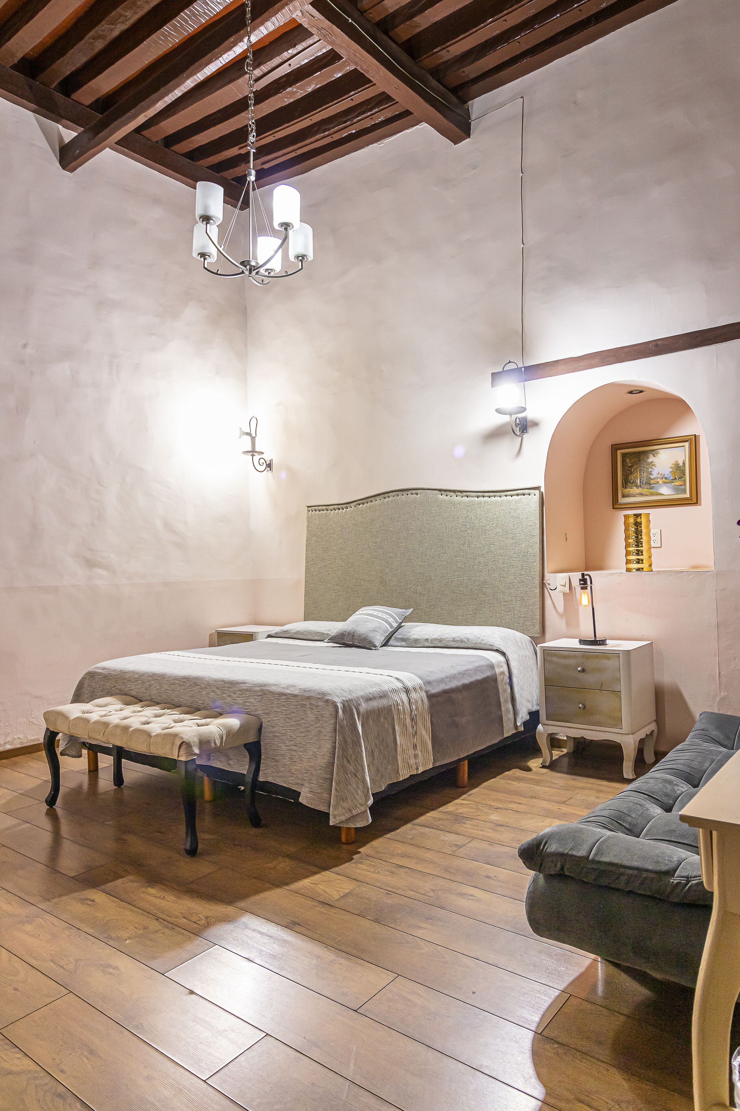 A bedroom with a bed, bench, nightstand, and a couch.