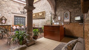 A historic interior with stone walls, a reception desk, a sofa, and potted plants. - Hotel Cantera Rosa (Morelia)