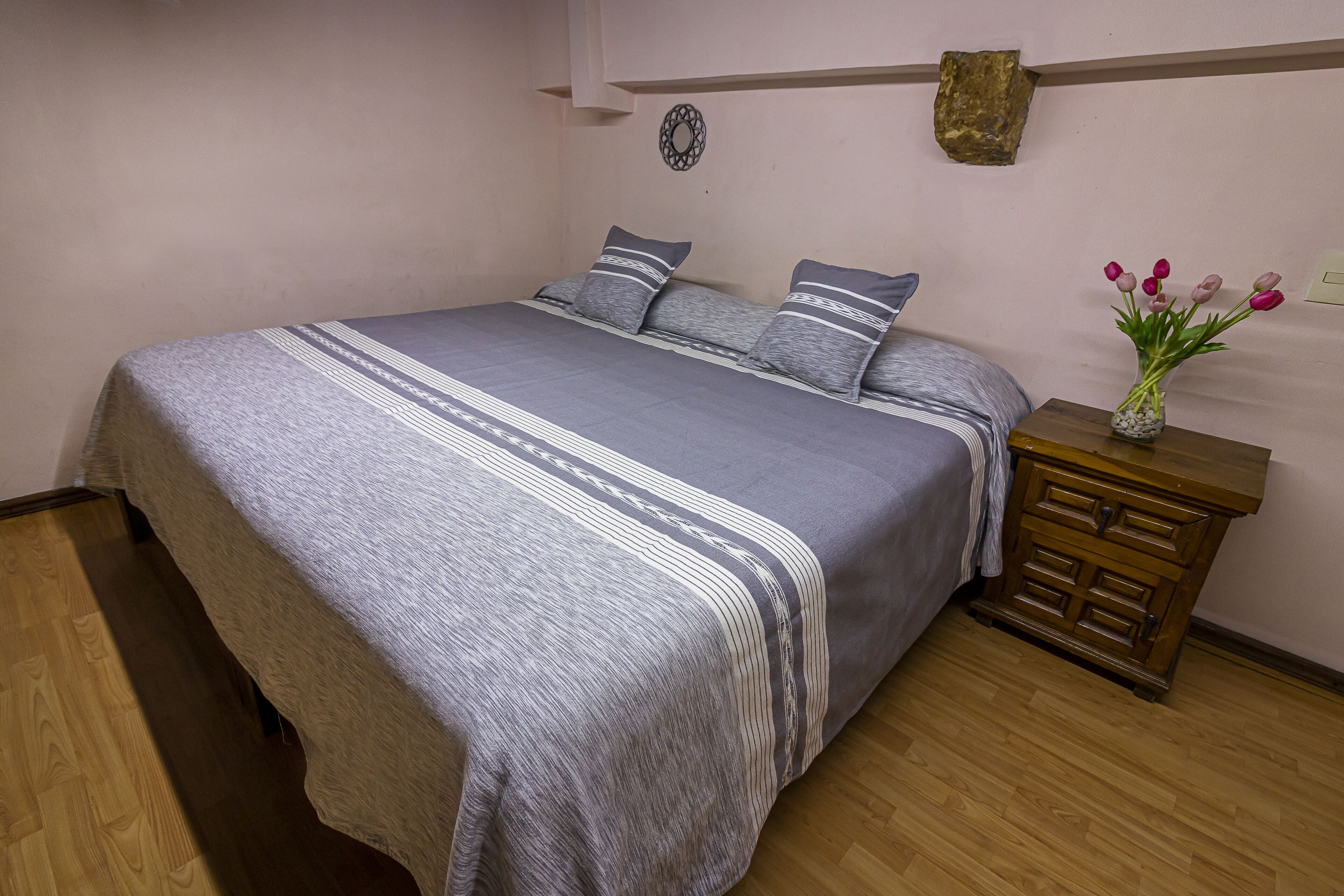 A bedroom with a bed, pillows, a bedside table, and a vase with flowers.