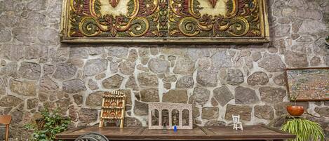 A stone wall with a decorative panel, a small table with figurines, and a potted plant.