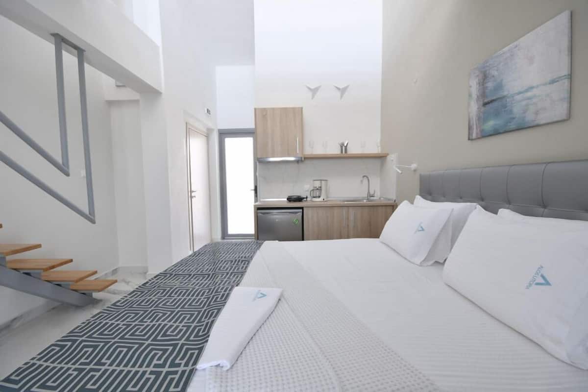 A modern hotel room with a large bed, a built-in desk, and a kitchenette.