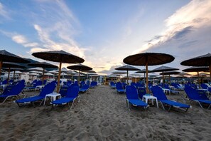 Ein Strand mit blauen Liegestühlen und reetgedeckten Sonnenschirmen, der an einen Strandort erinnert.