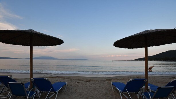 A beach with two umbrellas and blue lounge chairs. - Alos Utopia (Volvi)