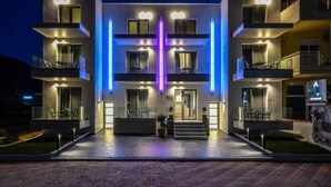 A modern building with multiple balconies, a central entrance, and outdoor seating areas. - Alos Utopia (Volvi)