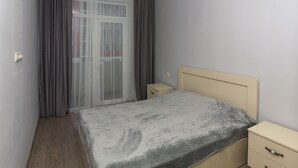 Une chambre à coucher avec un lit, une table de chevet, une commode et une fenêtre avec des rideaux.