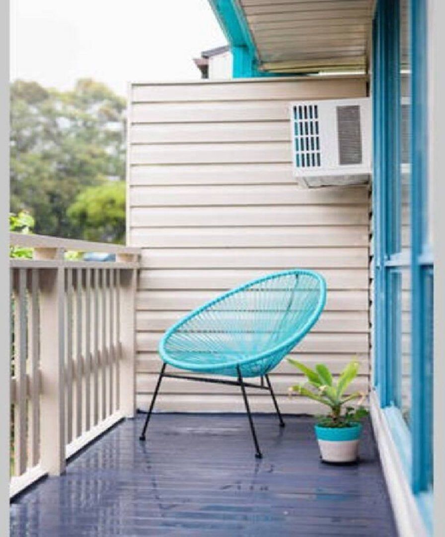 Ein Balkon mit einem türkisfarbenen Stuhl, einem Blumentopf und einem Fenster mit Jalousien.