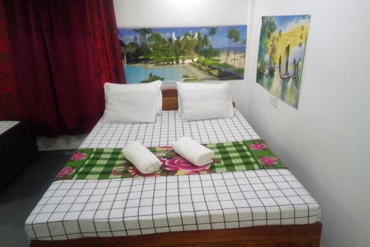 A neatly made bed with a checkered bedspread, two pillows, and rolled towels.