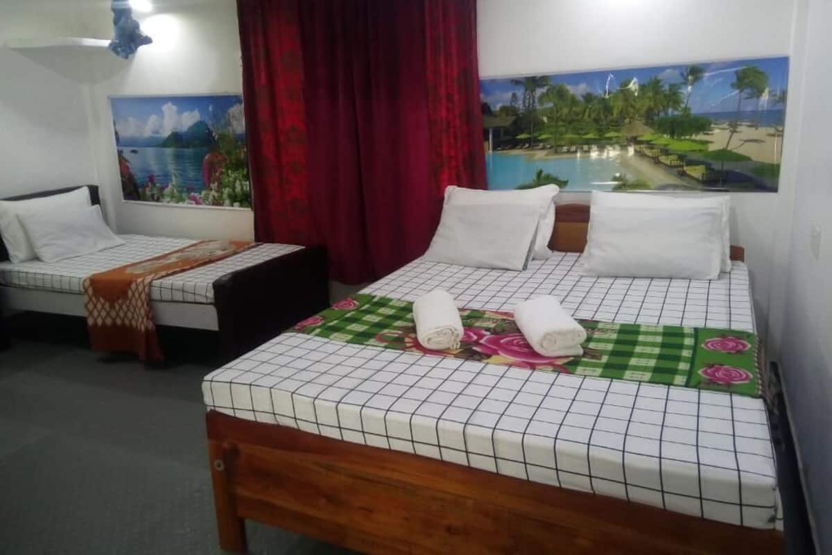 Une chambre d’hôtel avec deux lits, une grande fenêtre donnant sur la plage et un ventilateur de plafond.