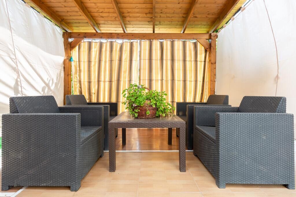 Un espace extérieur aménagé, abrité et doté de meubles en osier et d’une table, avec une plante en pot.