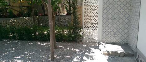 A courtyard with a stone wall, a pergola with yellow leaves, and a tiled shower area.