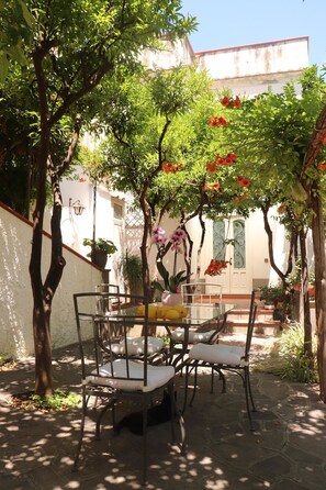 An outdoor patio with a table and chairs, surrounded by trees and potted plants. - Casa Amorino (Minori)
