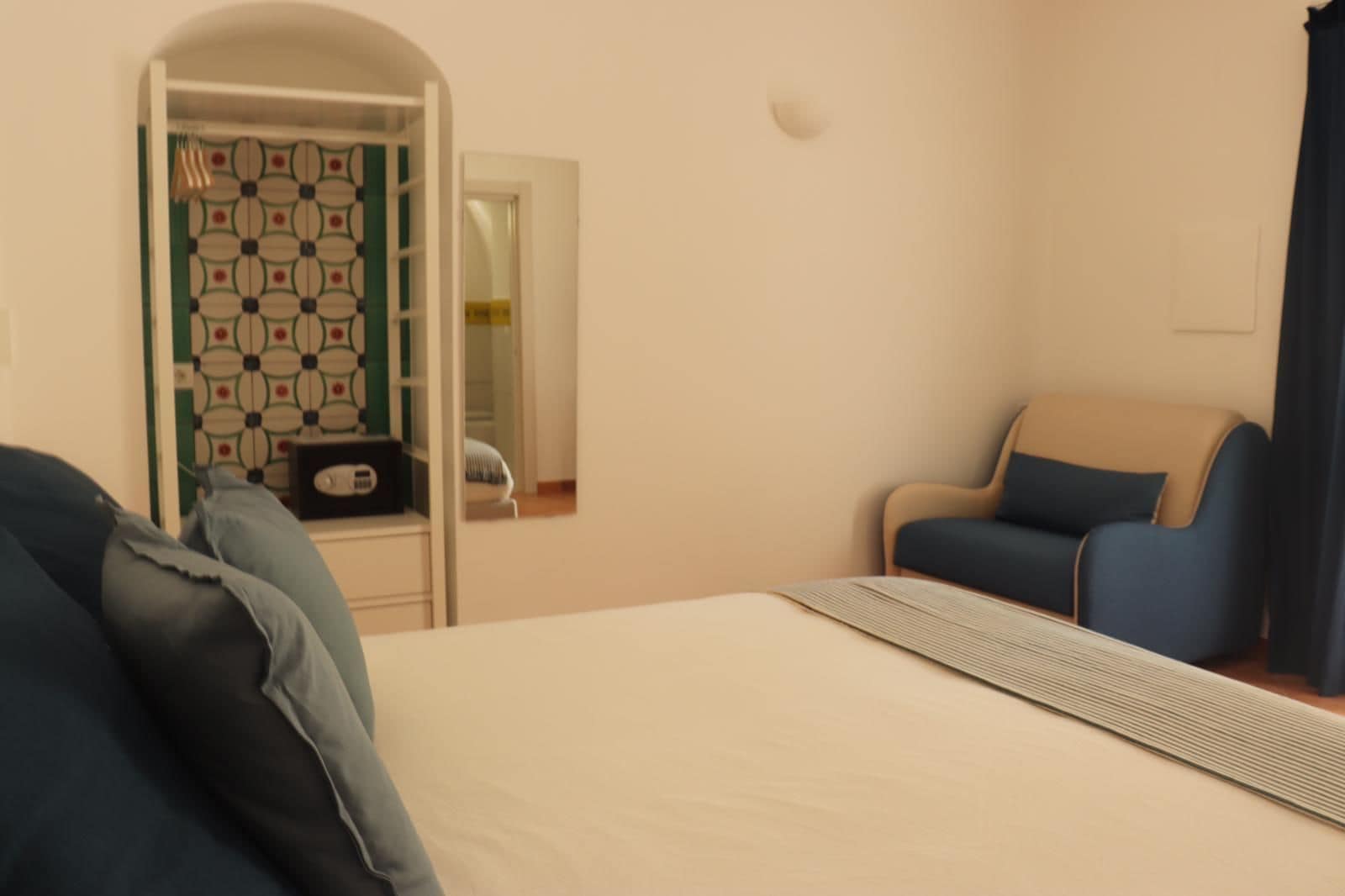 A hotel room with a bed, a chair, a small table, and a door leading to a bathroom.