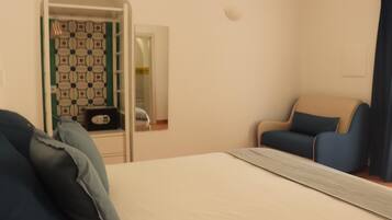 A hotel room with a bed, a chair, a small table, and a door leading to a bathroom.