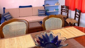 A living room with a sofa, chairs, a dining table with a blue glass centerpiece, a bookshelf, and a framed painting. - Quinto Sol 2 Departamento (San Miguel de Allende)