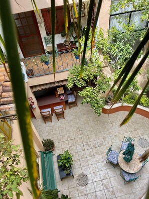 Een terras buiten met betegelde vloer, verschillende zithoeken en diverse potplanten.