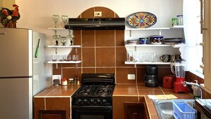 A kitchen with a stove, oven, and various kitchen items on shelves. - Quinto Sol 2 Departamento (San Miguel de Allende)