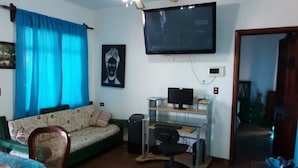 A living room with a sofa, a TV mounted on the wall, a computer desk with a chair, and a dining table with chairs. - Quinto Sol 4 Departamento (San Miguel de Allende)