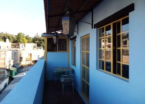 A small balcony with a table and chairs, a hanging lantern, and a view of neighboring buildings.