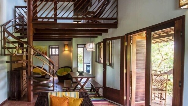 A spacious interior with a wooden staircase, a dining area, and a view of the outdoors. - Pipa Casa Cândido (Tibau do Sul)
