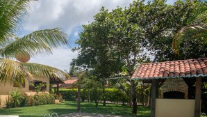 A swimming pool with a tiled deck, surrounded by lush greenery and a brick structure. - Pipa Casa Cândido (Tibau do Sul)