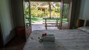 A room with a bed, a small table, and a view of a garden. - Pipa Casa Cândido (Tibau do Sul)