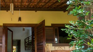 A covered outdoor area with a wooden table and chairs, a spiral staircase, and a door leading to an interior space. - Pipa Casa Cândido (Tibau do Sul)