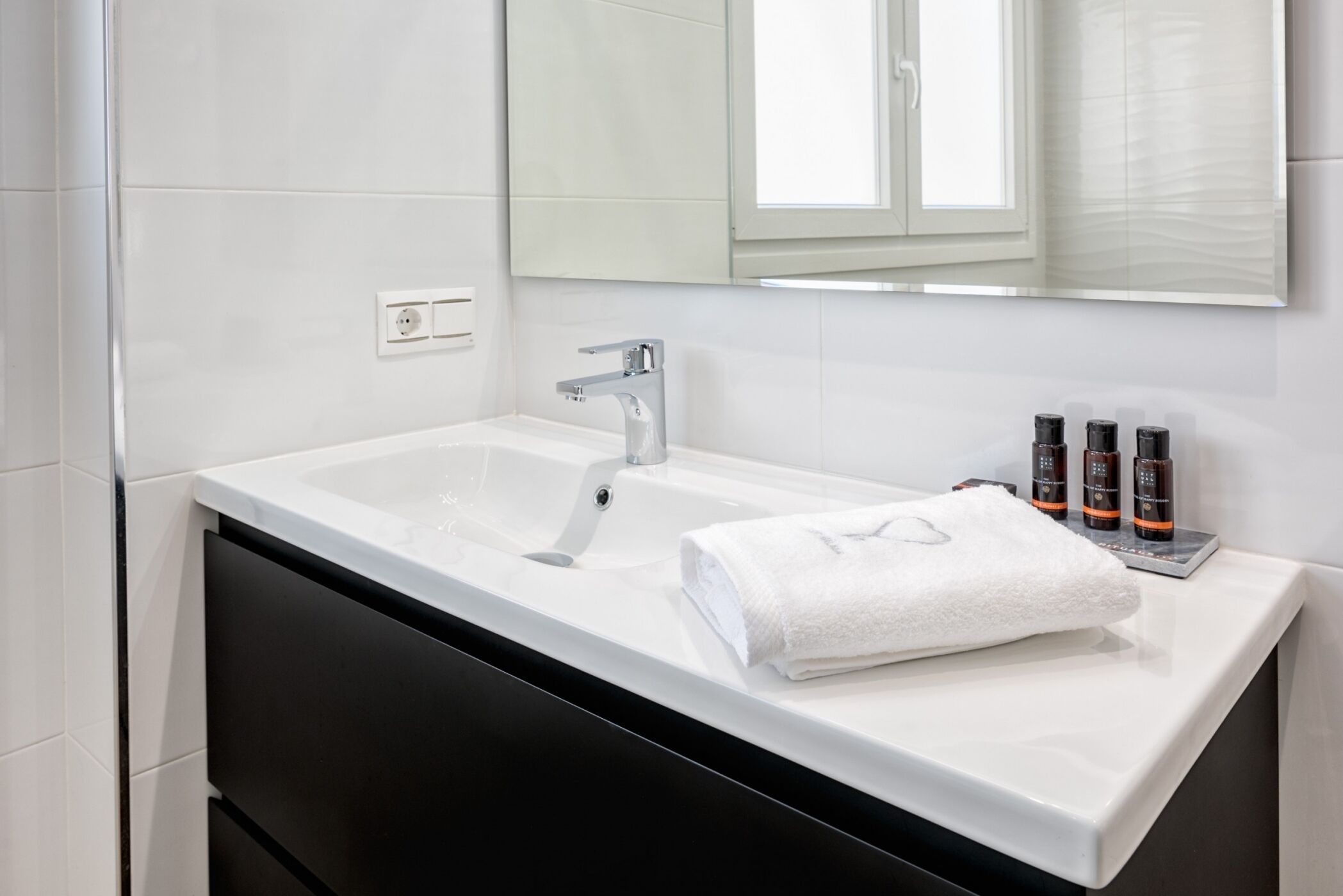Ein modernes Badezimmer mit einem weißen Waschbecken, einem schwarzen Schrank und einem großen Spiegel darüber.