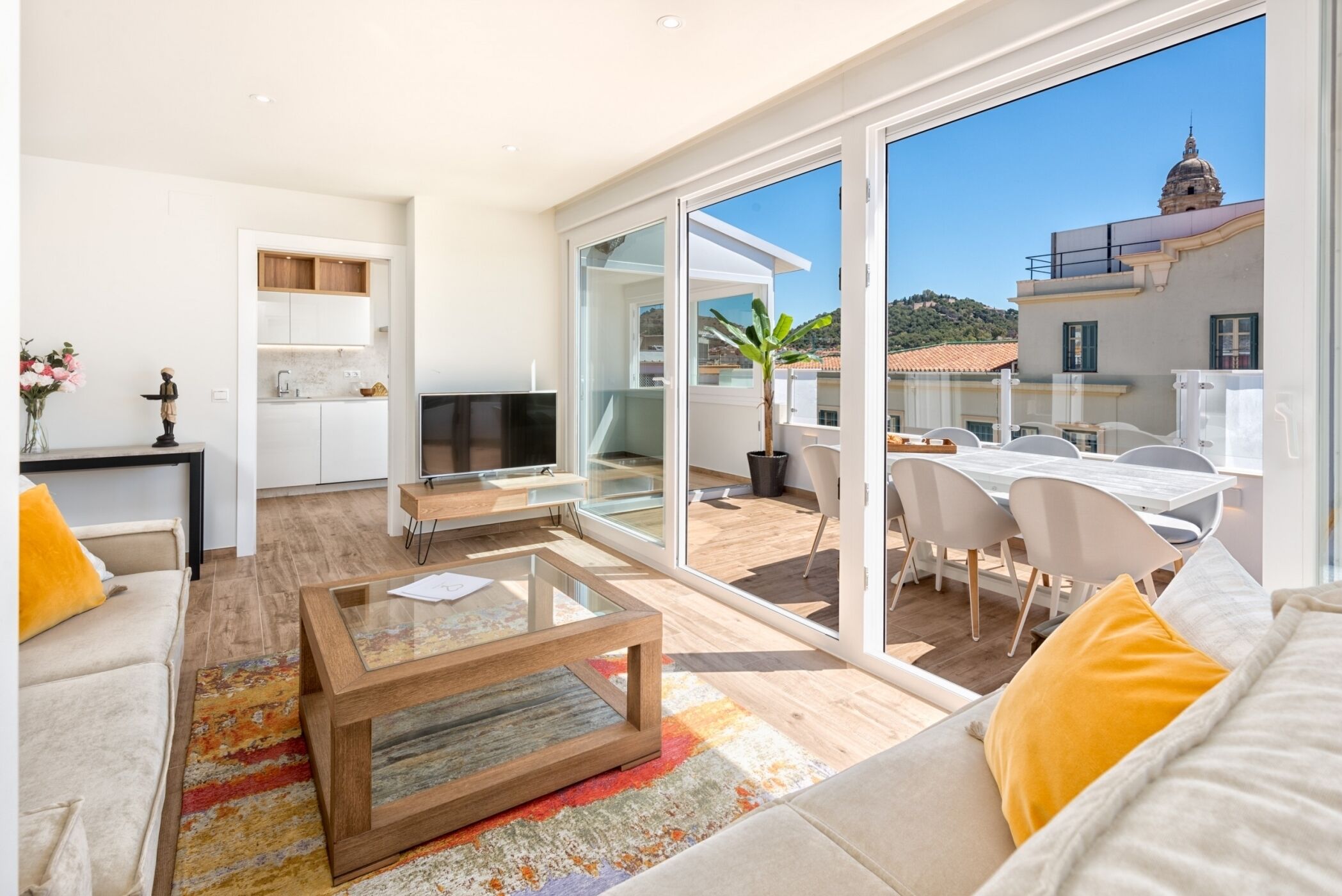 A modern living room with a sofa, coffee table, and a view of the city through large glass doors.