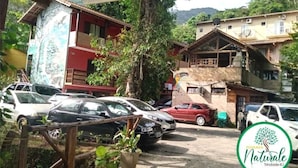A parking area with several cars, a building with a red facade, and a sign for 'Bousada Natural'. - Pousada Naturale (Paraty)