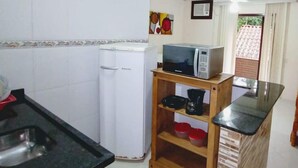A compact kitchen with a white refrigerator, a microwave on a wooden shelf, and a sink. - Pousada Naturale (Paraty)