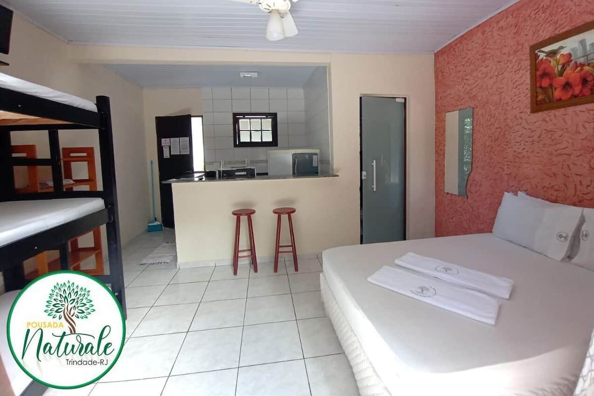 A hotel room with a bed, a desk, a kitchenette, and a ceiling fan.