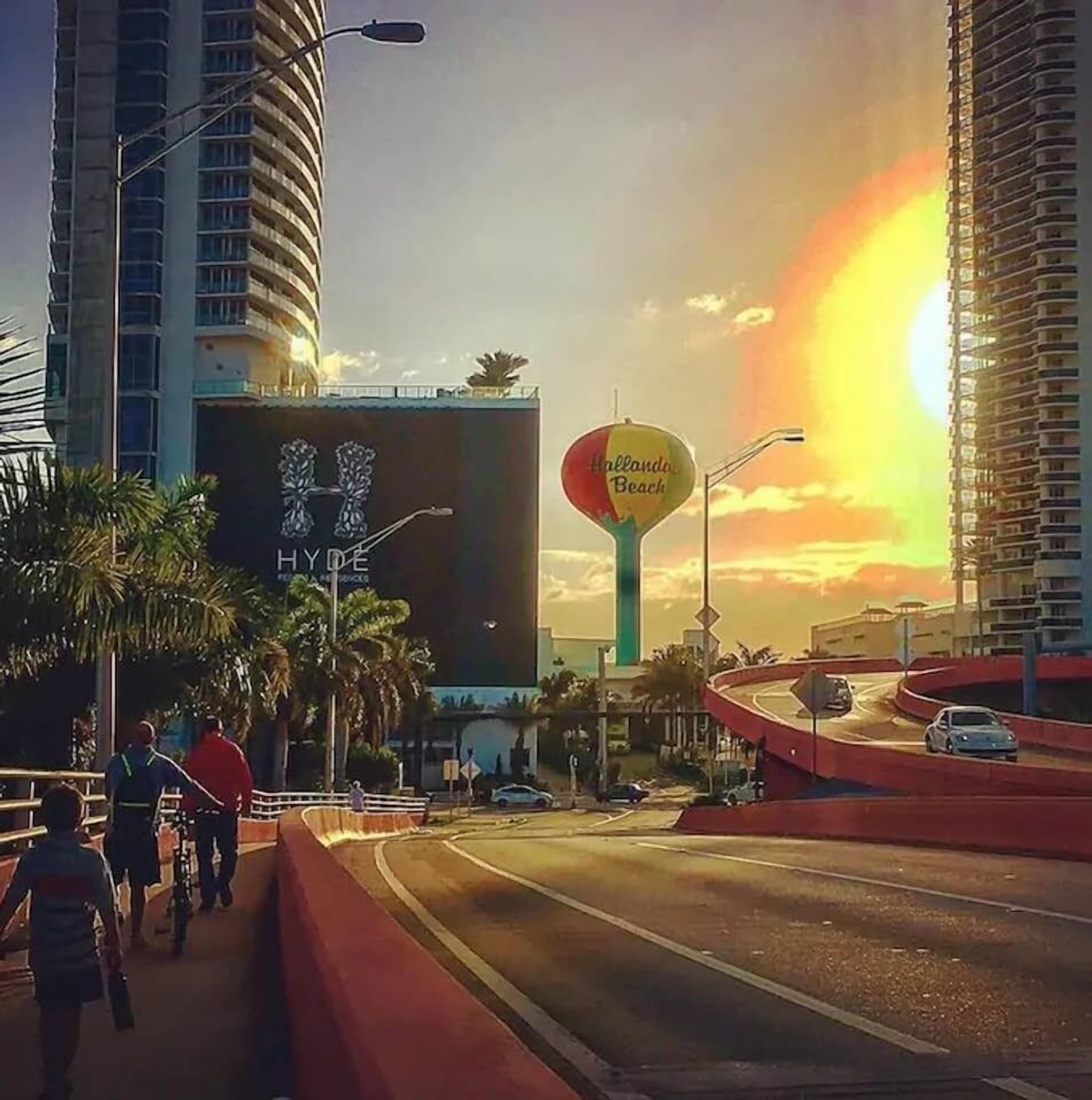 A city street with tall buildings, a large billboard, and a sunset.