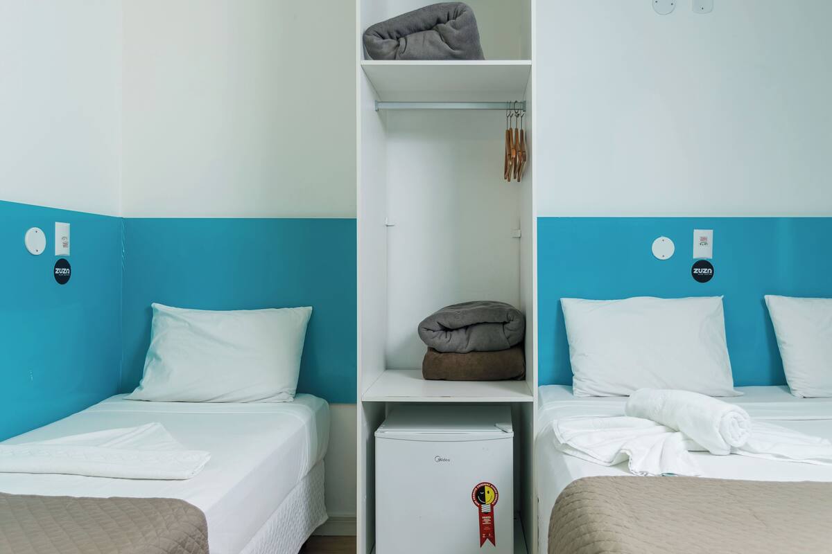 A hotel room with two beds, a wardrobe, and a minibar.