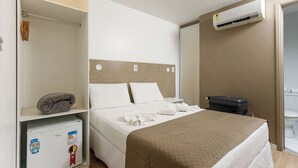 A hotel room with a bed, a small refrigerator, a suitcase, and an air conditioning unit. - Zuza Slim Suítes (Maceió)