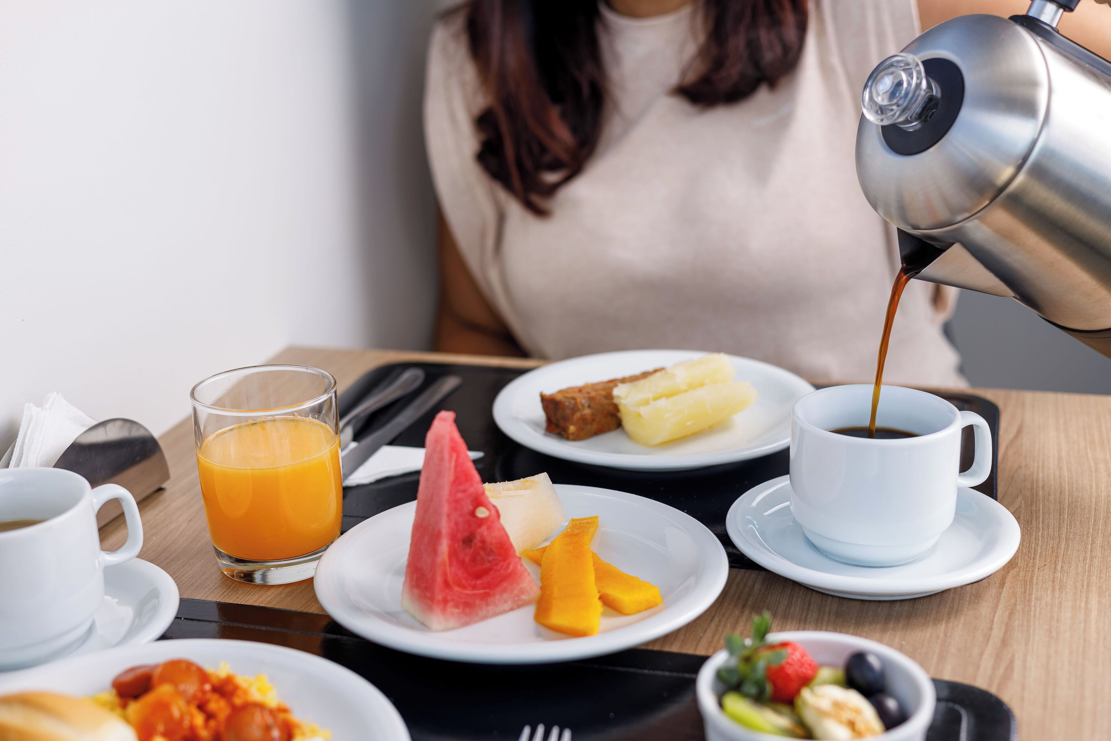 Una mesa de desayuno con platos de comida, un vaso de jugo de naranja y una taza de café que se está sirviendo.