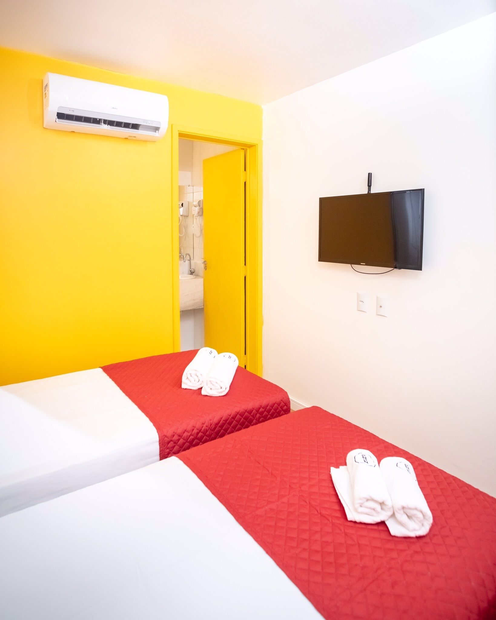 A hotel room with two beds, a TV, and an air conditioning unit.